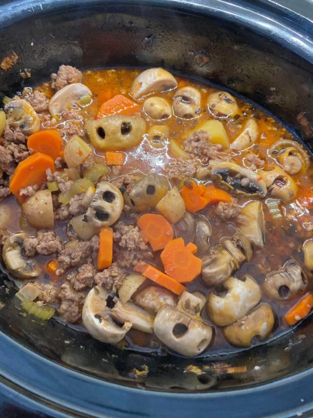 blue crockpost with soup ingredients - ground beef, carrots, mushrooms, and more. Full soup recipe linked.